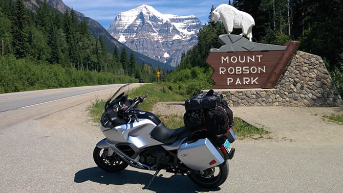 Picture of motorcycle parking in front of sign, mountains in background. 