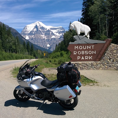 Picture of motorcycle parking in front of sign, mountains in background. 