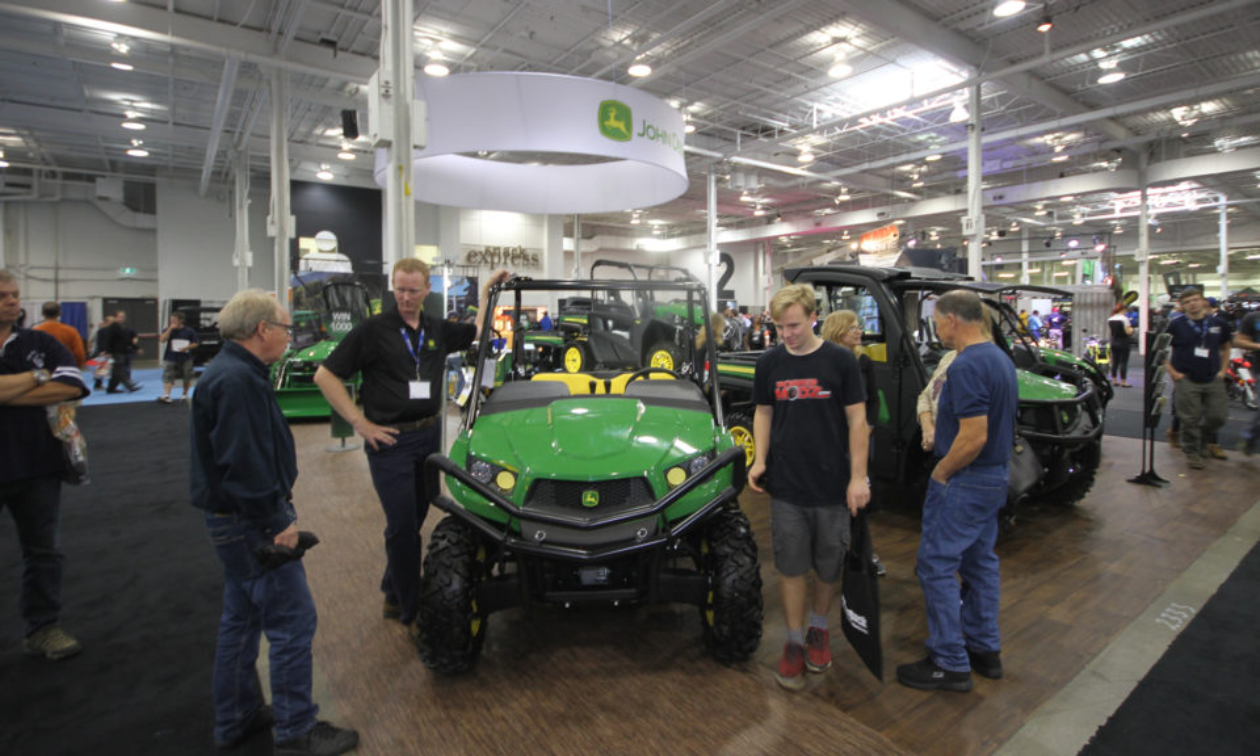 Attendees stand around a John Deere UTV inside of an events centre. 