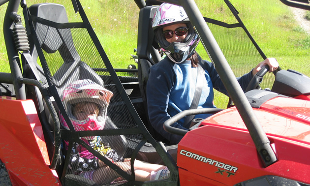 Photo of a women driving a UTV with her small daughter in the seat next to her. 