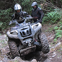 A woman on a green ATV riding up a steep trail. 