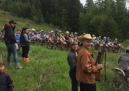 A group of riders on the starting line and a man holding a gun. 