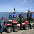 A group shot of a family standing with their red ATVs on a trail in the mountains. 