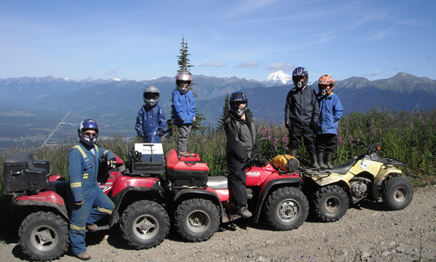 A group shot of a family standing with their red ATVs on a trail in the mountains. 