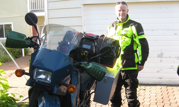 A man in yellow riding gear standing behind a dual-sport bike. 