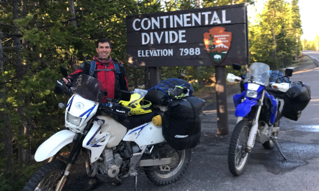 Graham Lindenbach poses next to dirt bikes and a sign for the Continental Divide.