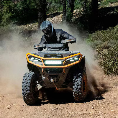 Someone wearing a helmet riding a Can-Am ATV through the woods, with the Can-Am logo and “explore the outdoors” in white font.
