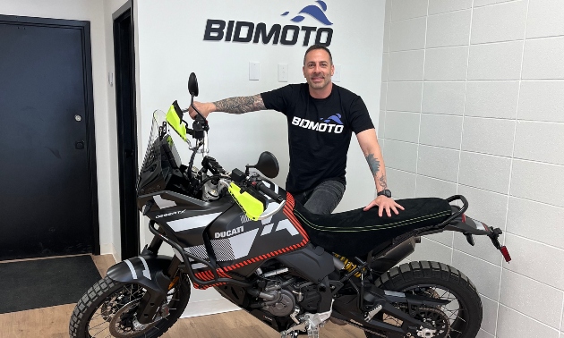 Chris Avarello standing next to a bike with BidMoto in the background