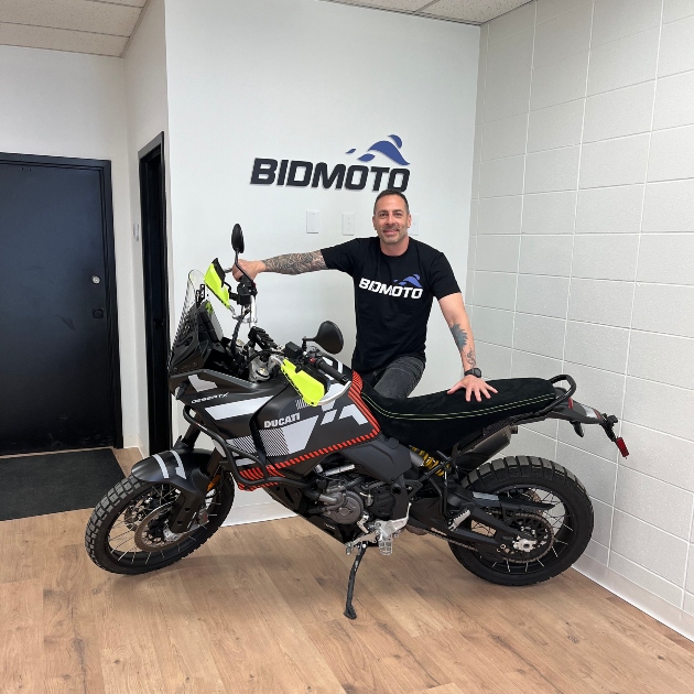 Chris Avarello standing next to a bike with BidMoto in the background