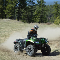 A guy on a green ATV going fast around a corner. 