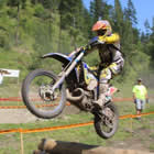 Photo of a guy jumping a dirt bike over a pile of logs on a dirt track. 