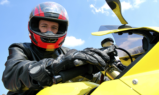 A man wearing a red and black helmet sitting on a yellow bike with the sky in the background. 