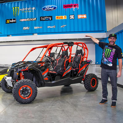 Ken Block standing beside his red and black Can-Am side-by-side. 