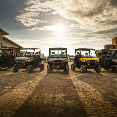 Five of Can-Am's new Defender utility side-by-sides lined up in a farmyard. 