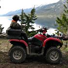 An ATVer sits on the back of a quad in front of a mountain lake