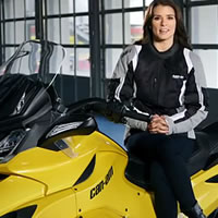 A woman with long brown hair sitting on a yellow Can-Am Spyder. 