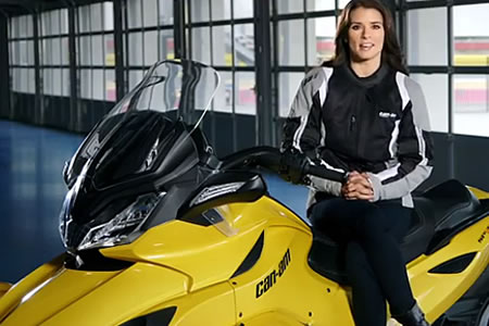 A woman with long brown hair sitting on a yellow Can-Am Spyder. 