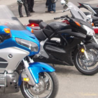 Photo of a blue bike, a black bike and several other bikes parked in a lineup in front of a dealership. 