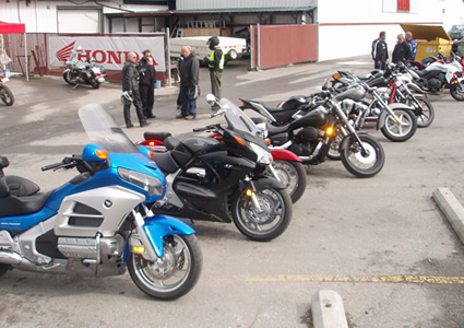 Photo of a blue bike, a black bike and several other bikes parked in a lineup in front of a dealership. 