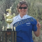 woman in blue and white jersey standing with a trophy in the desert. 