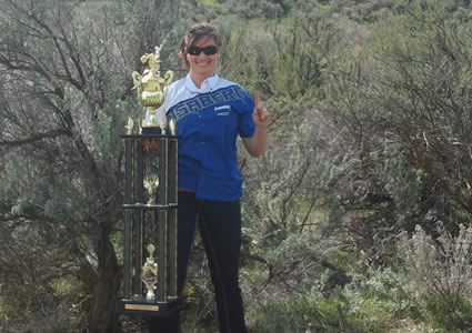 woman in blue and white jersey standing with a trophy in the desert. 