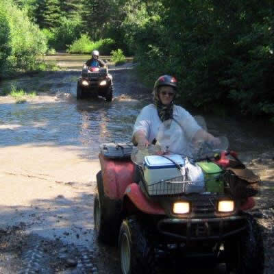 A woman on an ATV riding through a mud puddle. 