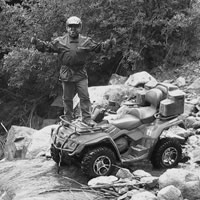 A man standing on the front of his quad in the backcountry. 