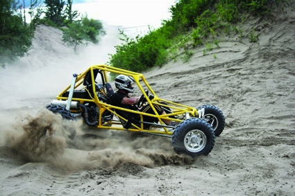 A dune buggy sprays a rooster-tail of sand as it tops out on a lakeside dune