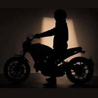 A person on a motorcycle in shadows. 