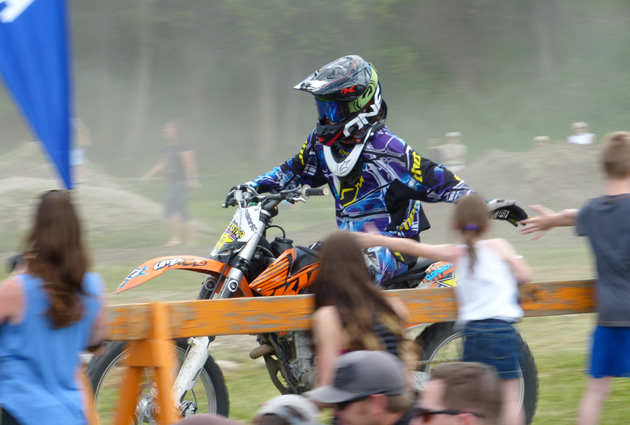 A man on a motocross bike slapping hands with kid spectators. 