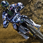 A guy in full riding gear on a blue motocross bike riding on a dirt track. 