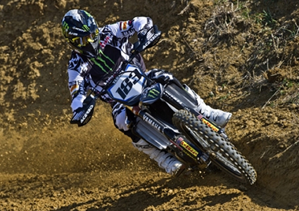 A guy in full riding gear on a blue motocross bike riding on a dirt track. 