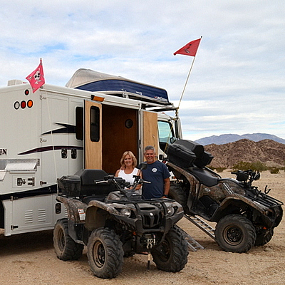 A man and woman standing by their modified toy hauler with ATVs. 