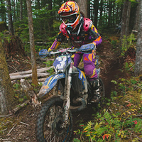 A woman riding a dirt bike through the forest. 