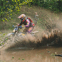 A woman splashing through a mud puddle on a dirt bike. 