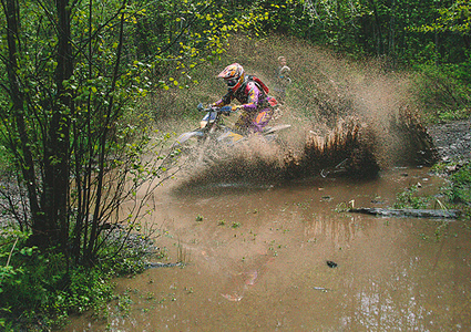 A woman splashing through a mud puddle on a dirt bike. 