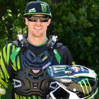 A man dressed in green moto gear standing beside a dirt bike. 