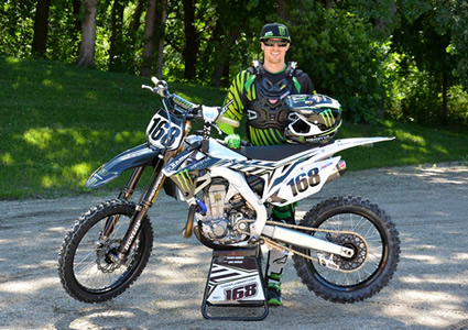 A man dressed in green moto gear standing beside a dirt bike. 