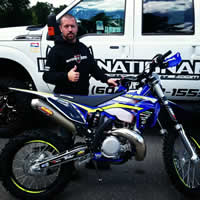 A middle-aged man standing behind a blue Sherco bike. 