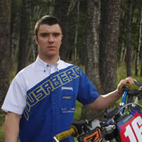 A young man in a blue and white husaberg shirt standing by a dirt bike. 