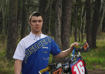 A young man in a blue and white husaberg shirt standing by a dirt bike. 