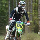 Photo of a guy dressed in black riding a green and yellow dirt bike. 