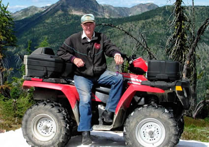 Photo of a man sitting on a red quad with the mountains in the background. 