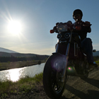 A silhouette of a guy on a motorcycle parked on a hill overlooking a river. 