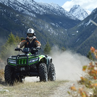 A man on a green ATV with the mountains in the background. 