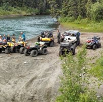 A group of ATVers parked along a river. 