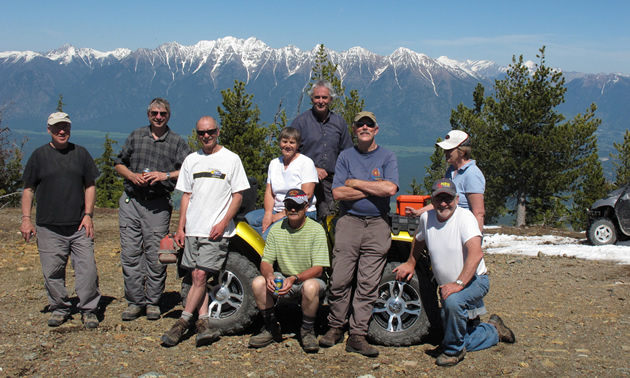 A group of people sitting together around a quad at the top of a mountain. 