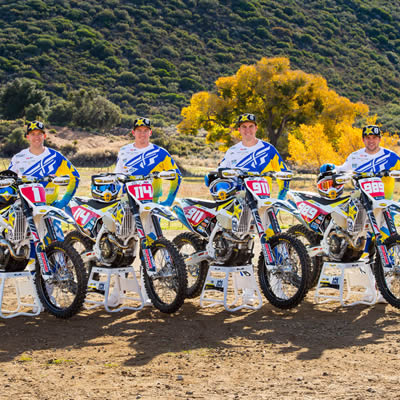 Four dirt bike riders lined up beside their bikes. 