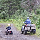 Man and a boy, each on an ATV, riding on a trail into the forest