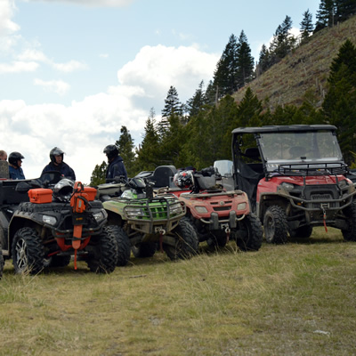 A group of ATVs or quads and a side by side parked in a row on a hilltop. 